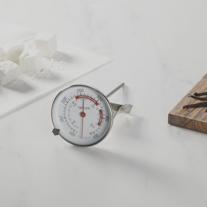 Candy and deep fry thermometer with large dial on a white surface beside a wooden cutting board