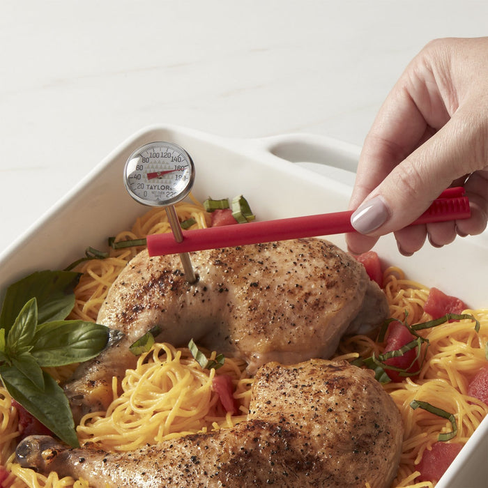 Hand holds a red instant read thermometer inserted into a roasted chicken on a bed of pasta