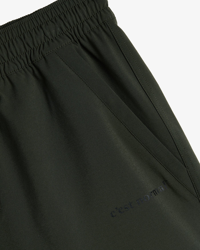 A close-up view of The Shorts in khaki, highlighting the elasticated waistband, side pocket, and the c'est normal logo printed on the fabric.