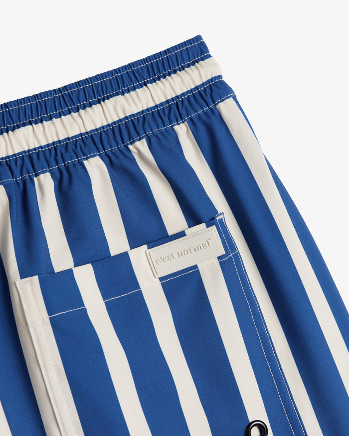 A detailed close-up of The Shorts in Nautical Stripe, laid flat on a white background. The image highlights the elastic waistband, the back pocket, and a rubber patch featuring the c'est normal logo.