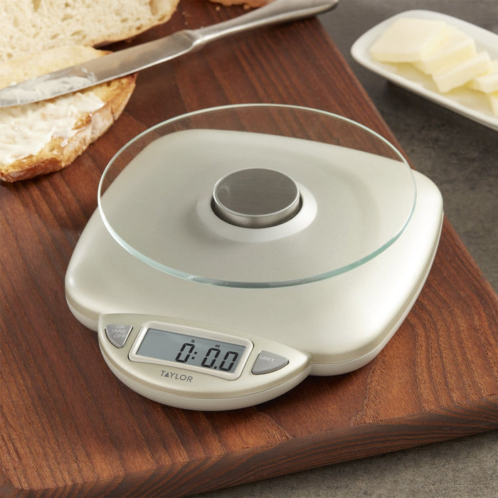 Digital kitchen scale with glass top on a wooden cutting board beside bread and butter.