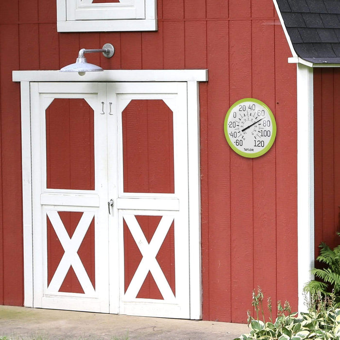 Green framed outdoor thermometer mounted on red barn siding beside white double doors