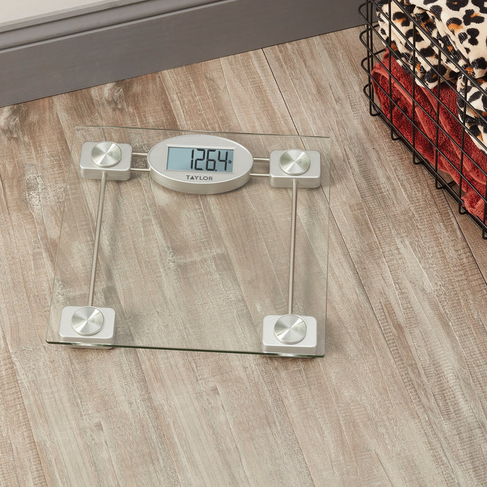 Glass platform digital bathroom scale on a wood floor shows 126.4 lb beside a laundry basket with leopard print blanket.