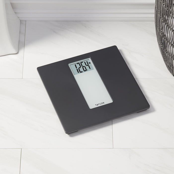 Dark gray digital bathroom scale on a light tiled floor with a white display showing 120.4 lb