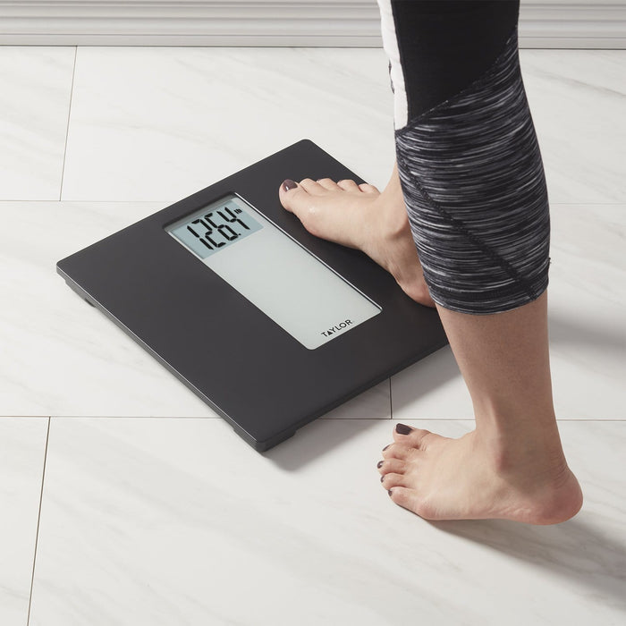 Person steps onto a dark gray digital bathroom scale on a white tiled floor