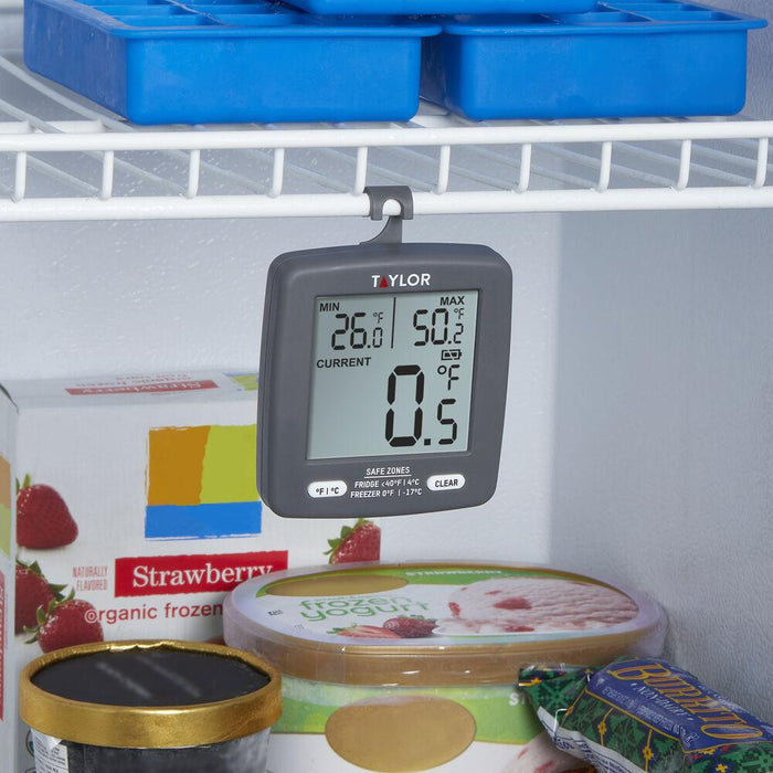 Taylor digital thermometer hanging from a fridge shelf among food, with min around 26 F max around 50 F on display.