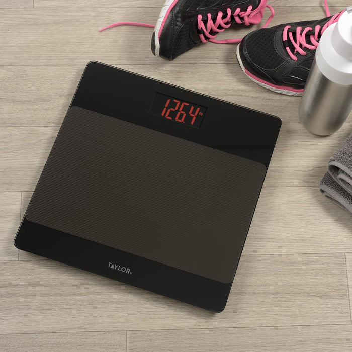 Black digital glass bathroom scale on a wooden floor with a red readout 126.4 lb and pink sneaker laces nearby