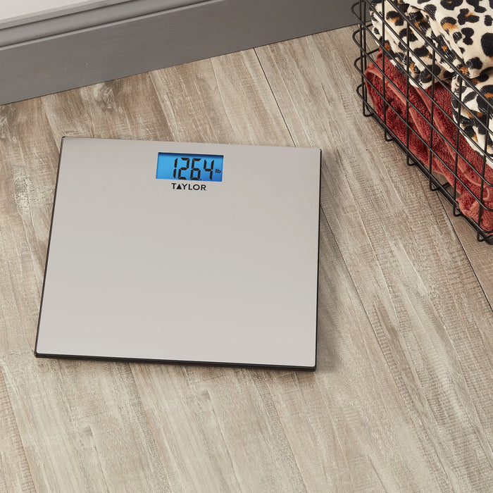 Digital stainless steel bathroom scale on a wood floor with a blue backlit display reading 126.4 lb beside a wire basket with a leopard print blanket.
