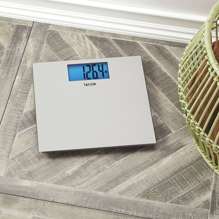 Top-down view of a digital textured stainless steel scale on a wooden floor with a pale green wicker basket nearby.