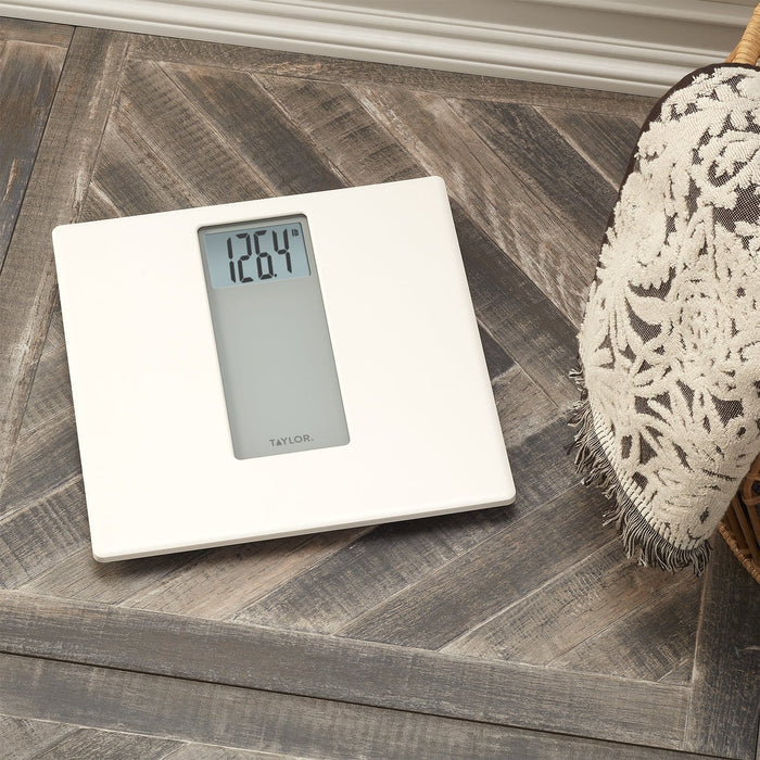 White digital bathroom scale on a wood floor beside a woven fringe rug