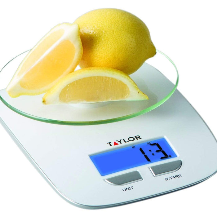 Lemons on the glass platform of a digital kitchen scale, a whole lemon and a lemon wedge.
