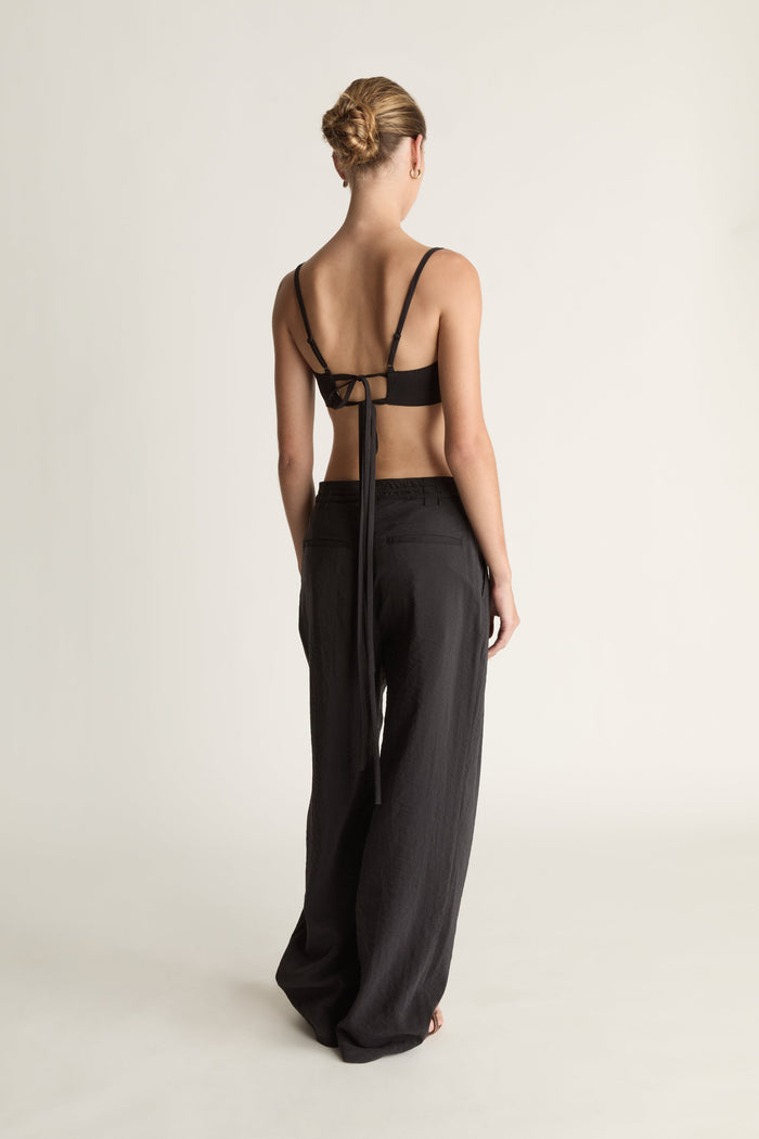 Woman wearing a cropped black top and wide-leg pants on a plain background