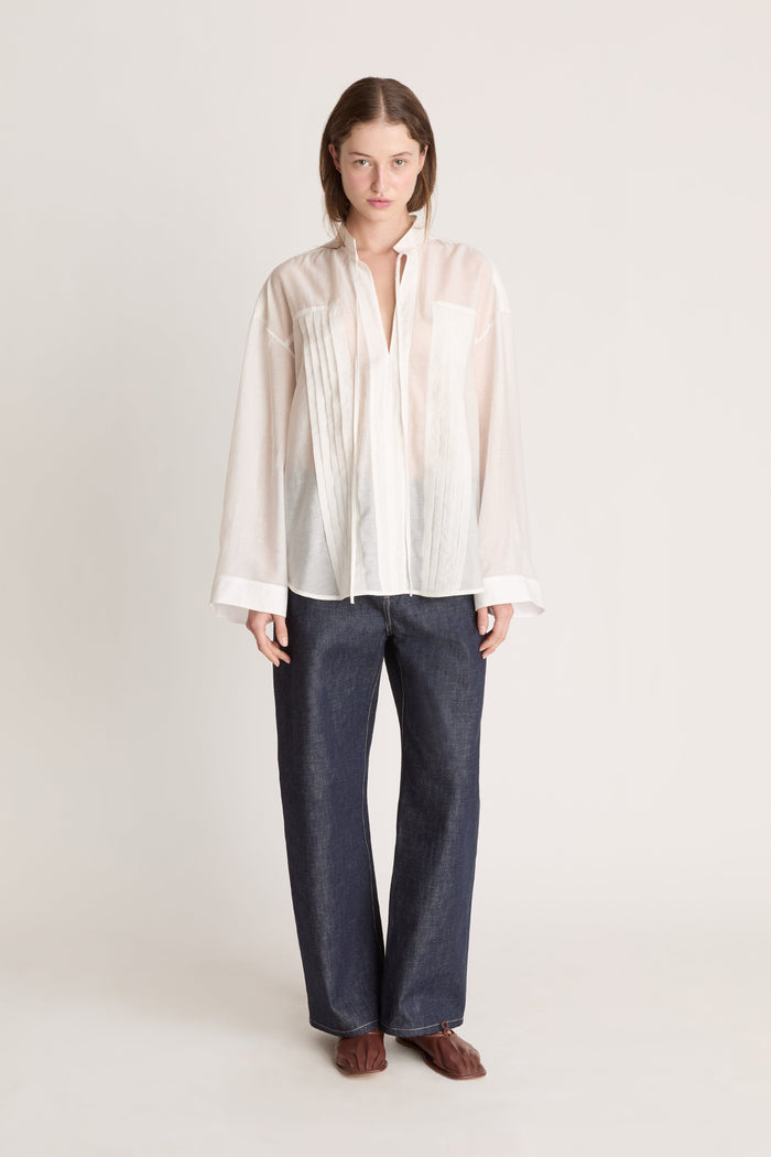 Person wearing a light-colored blouse and dark pants on a white background