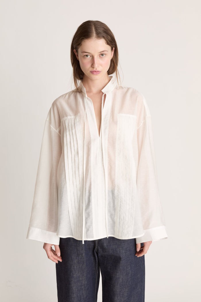 Person wearing a light-colored blouse and dark pants on a white background
