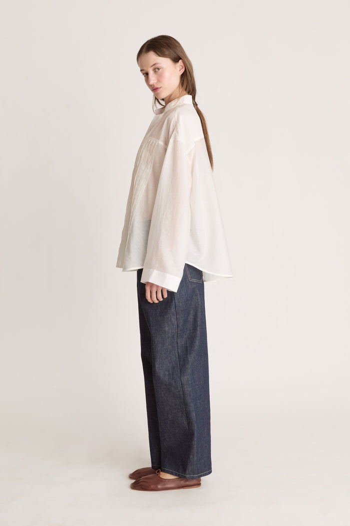 Person wearing a light-colored blouse and dark pants on a white background
