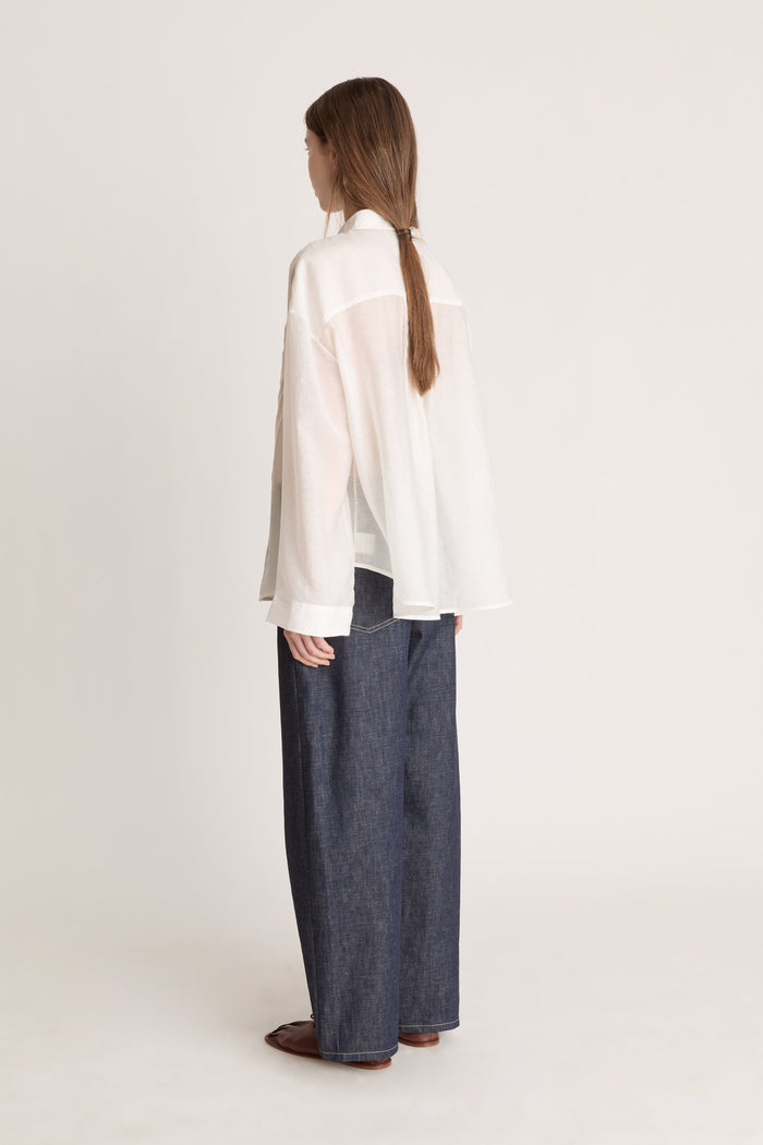 Person wearing a light-colored blouse and dark pants on a white background