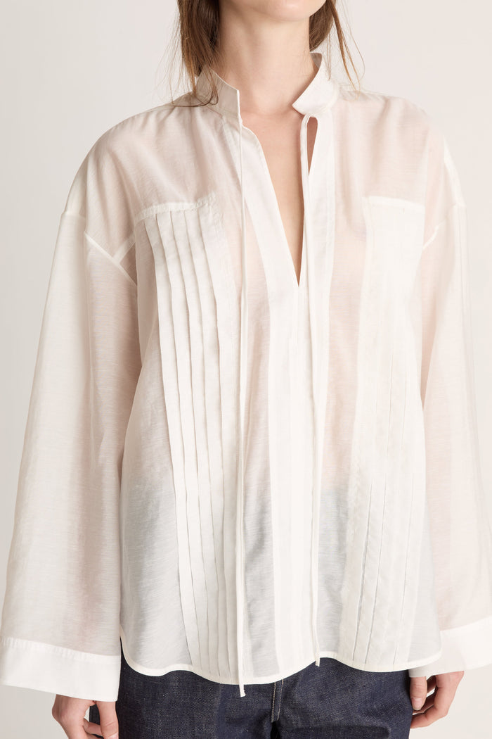 Person wearing a light-colored blouse and dark pants on a white background