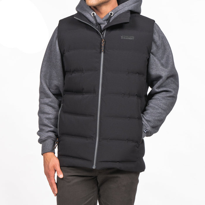 A person wearing a black down insulated vest with YKK zips, handwarmer pockets, and made from recycled plastic bottles fabric.