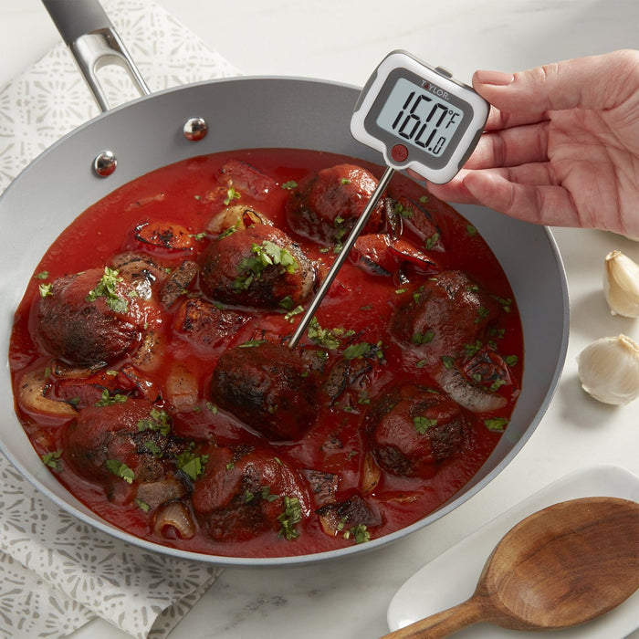 Thermometer probe inserted into meatballs simmering in tomato sauce in a pan