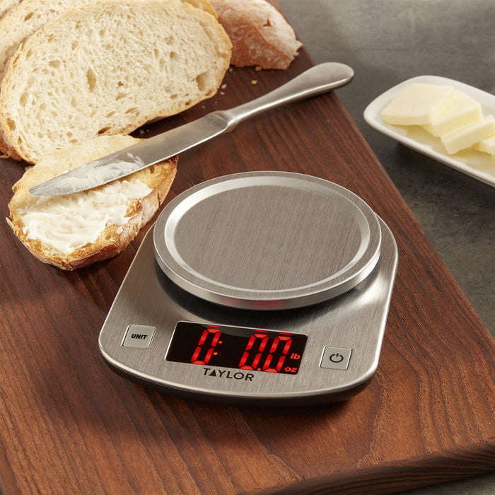 Bread slices with butter on a cutting board and a stainless steel kitchen scale in the foreground.