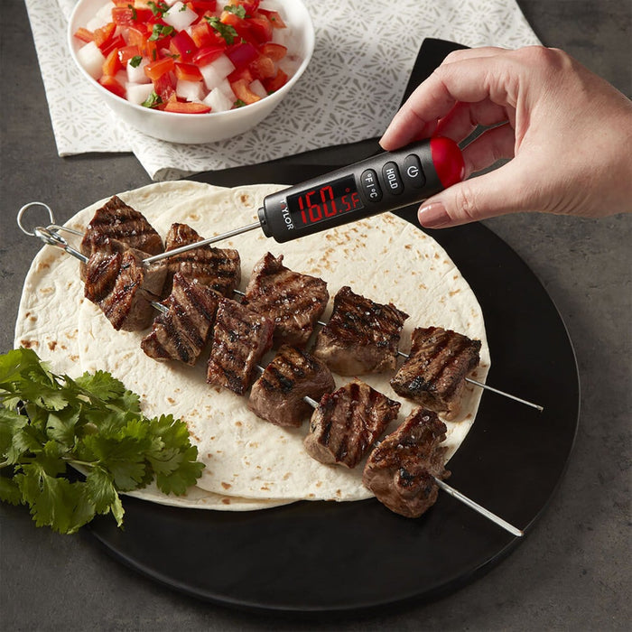 Handheld LED thermometer inserted into skewered grilled beef on a tortilla on a black plate