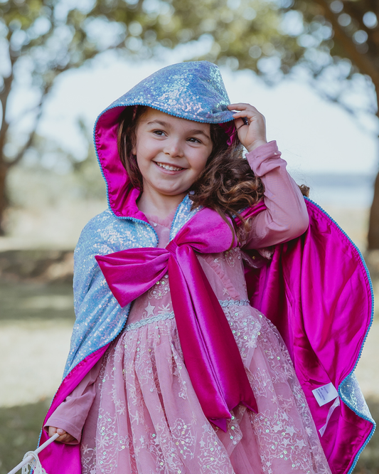 Child wearing a blue sequin hooded fairy godmother cape with a magenta lining