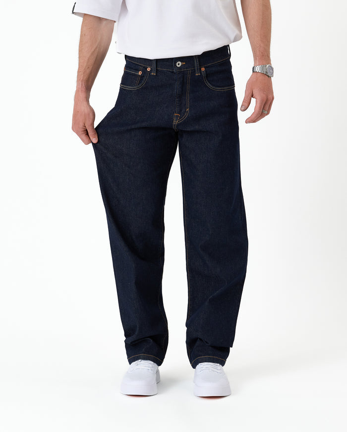 The Jeans Relaxed Straight Fit in rinse wash — pulled to show the stretchy fabric