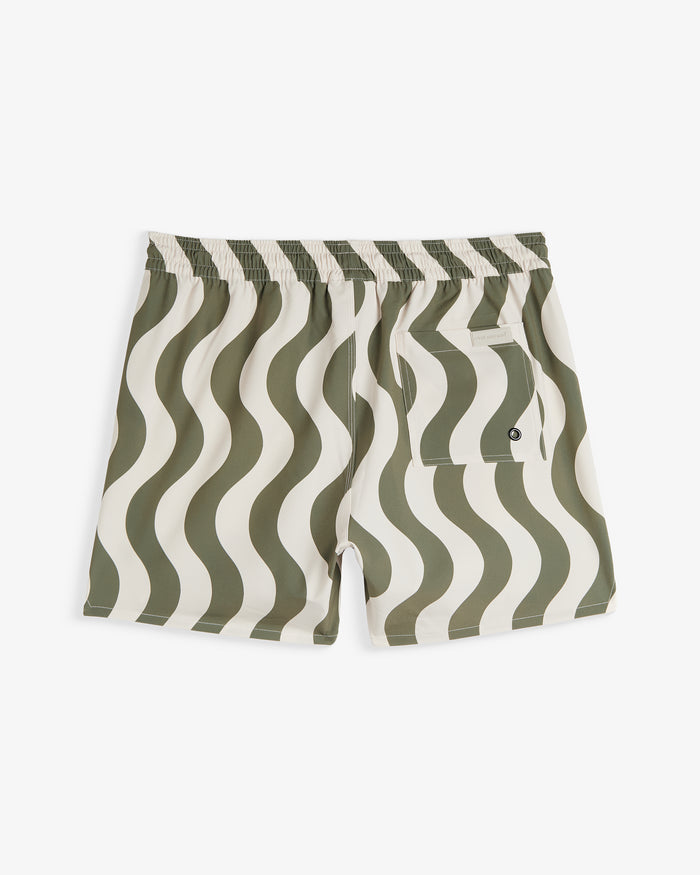 A back view of The Shorts in an olive curl stripe pattern, laid flat on a white background. The image highlights the elasticated waistband, a back pocket with a drainage eyelet, and a small c'est normal logo tag.