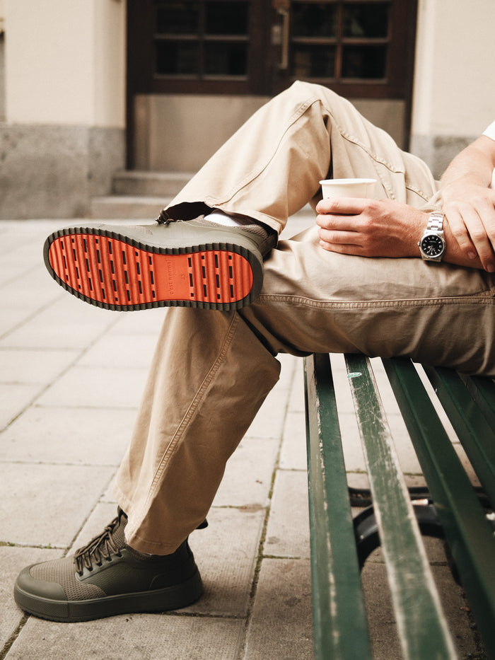 The Sneakers 2.0 in khaki — showing the orange rubber grid sole while sitting on a bench