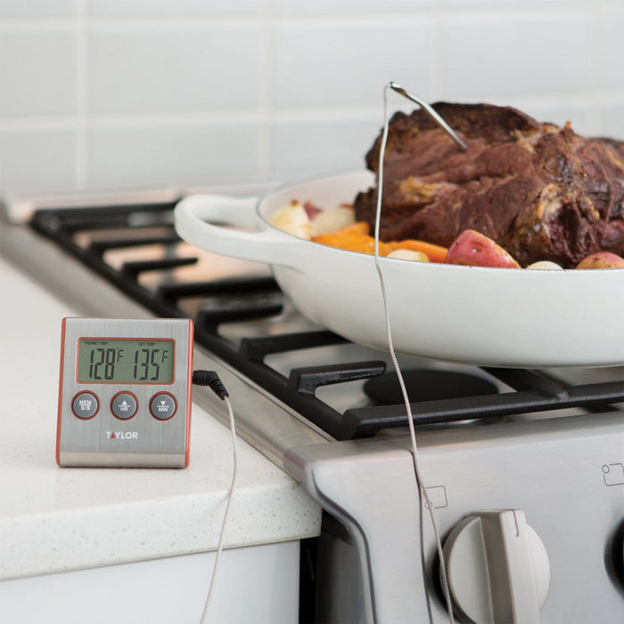 Wired probe thermometer with digital display beside a roasting pan on a gas stove